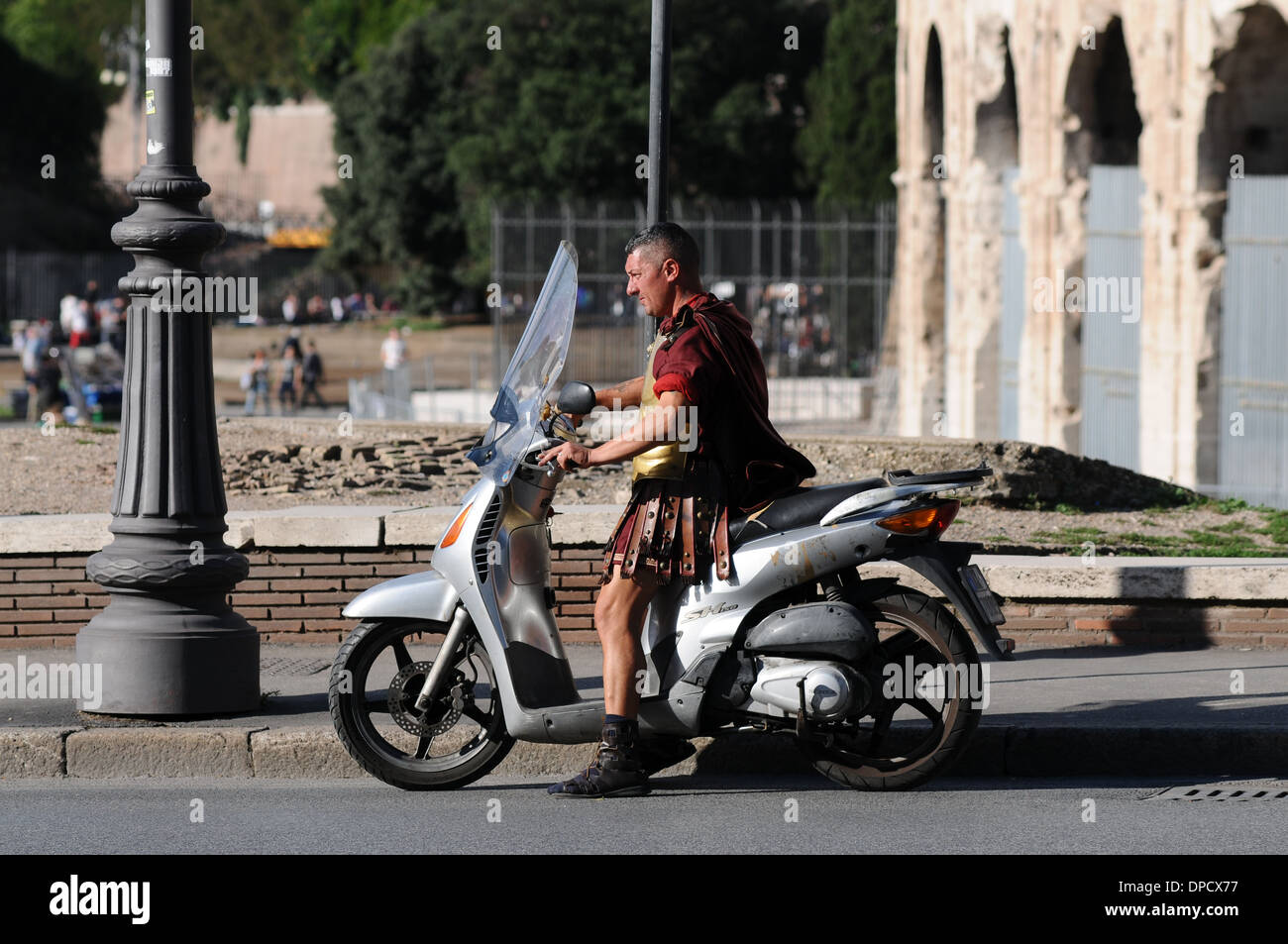 Un soldato romano seduto su un ciclomotore al di fuori il Colosseo a Roma, Italia. Il Colosseo è in costruzione. Foto Stock