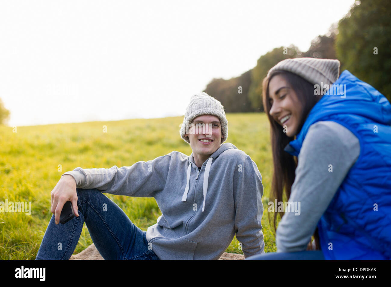 Coppia giovane seduto sull'erba ridere Foto Stock