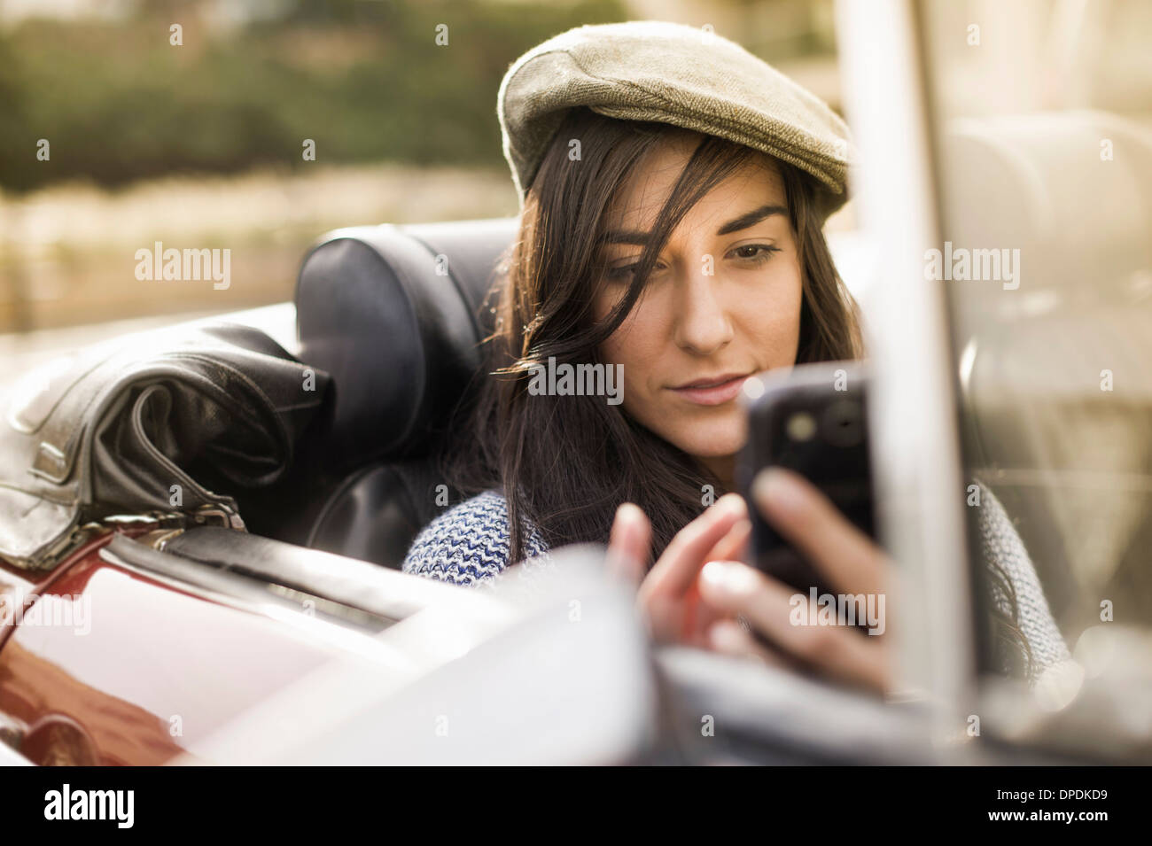 Giovane donna che indossa il tappo piatto nel convertibile utilizza lo smartphone Foto Stock