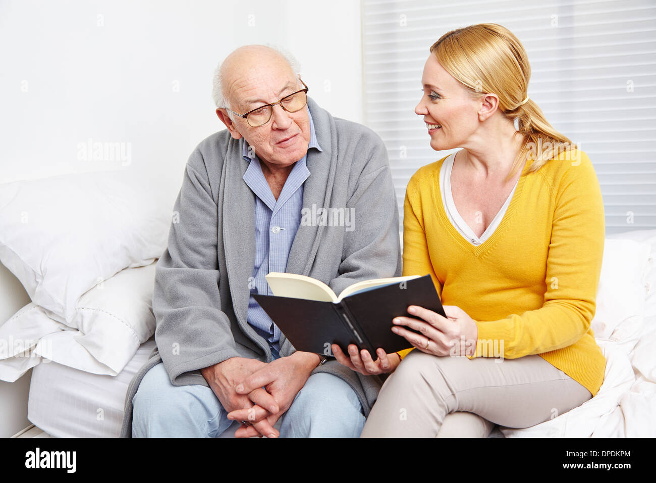 La donna la lettura di un libro di un anziano uomo in casa di cura Foto Stock