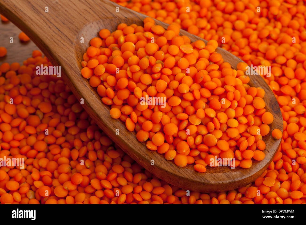 Di lenticchie rosse sul cucchiaio di legno sul rosso sfondo di lenticchie Foto Stock