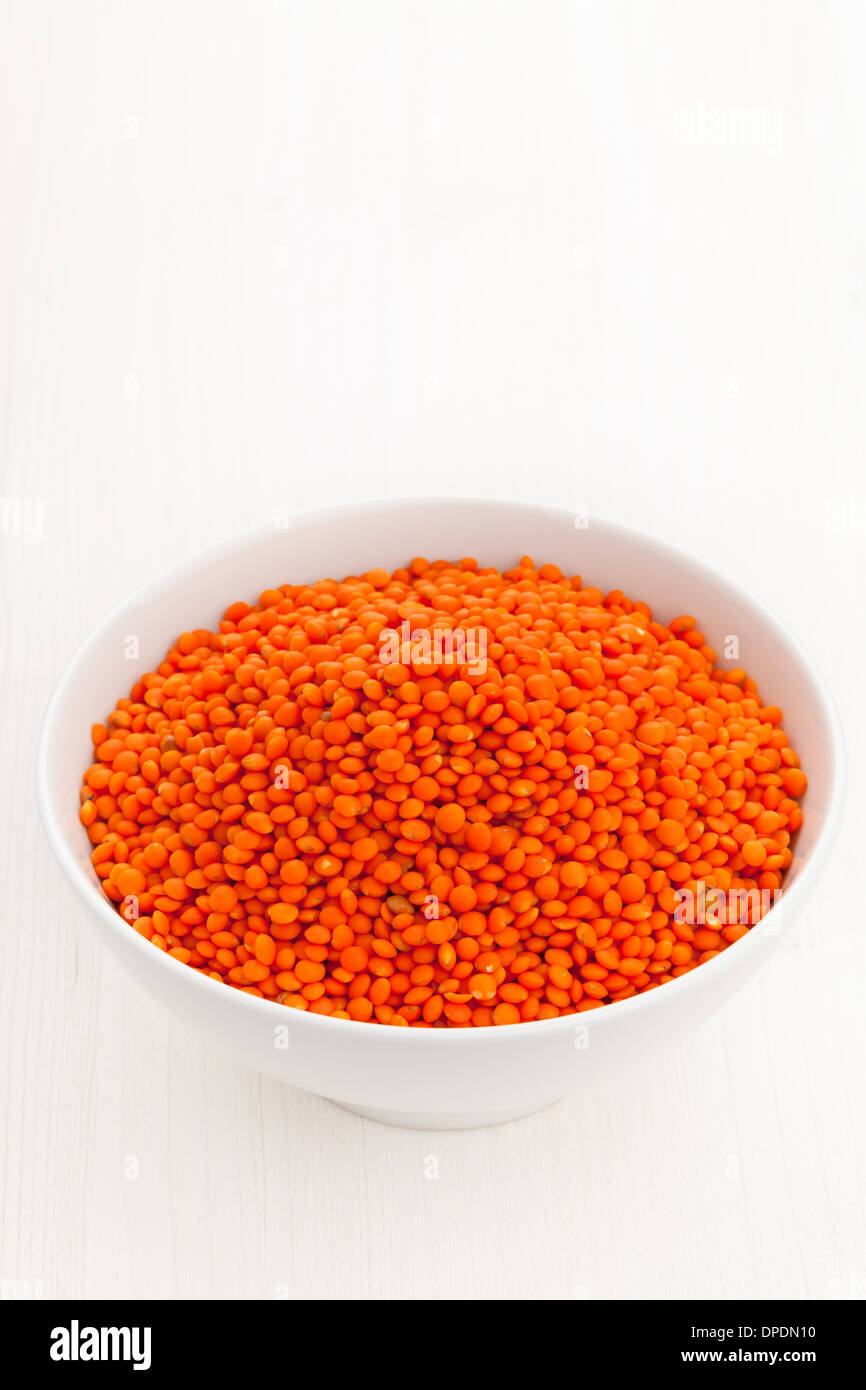 Di lenticchie rosse nella ciotola bianco su bianco sullo sfondo di legno Foto Stock