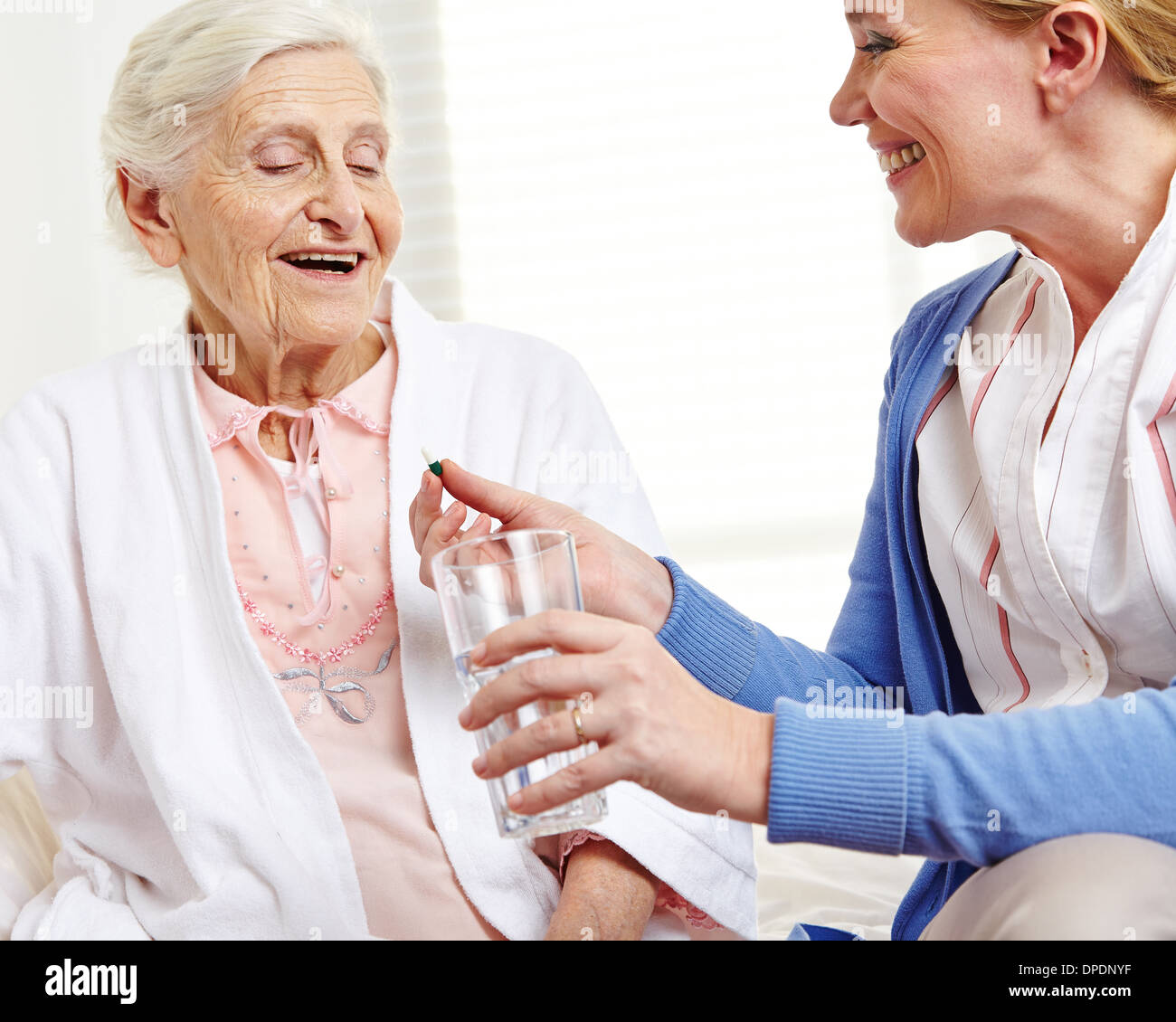 Senior donna prendendo la pillola con acqua da infermiera geriatrica Foto Stock