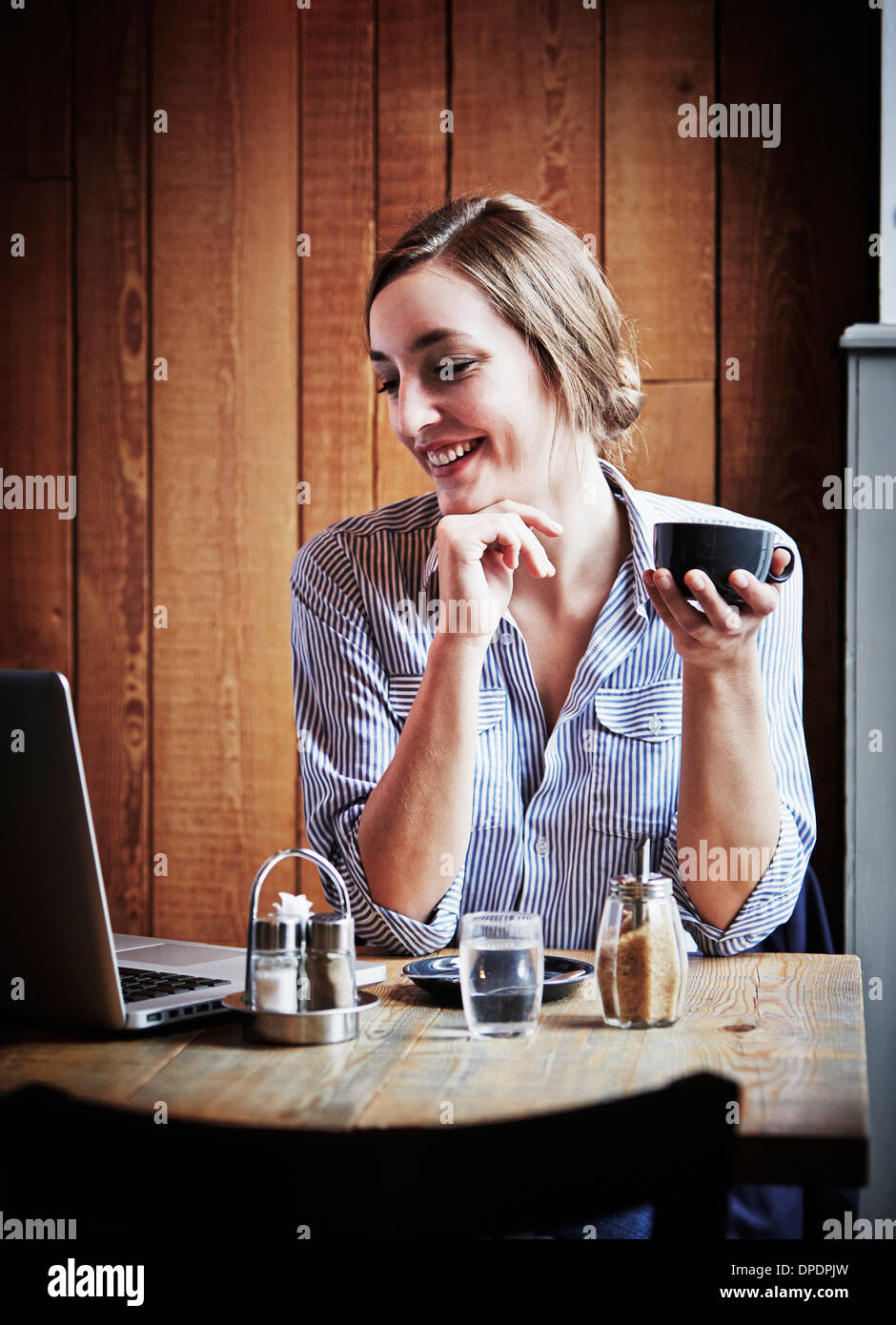 Giovane donna seduta al cafe azienda bevanda calda, utilizzando il computer portatile Foto Stock