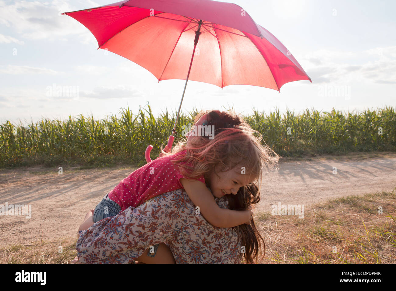 Madre e figlia abbracciando sotto ombrellone rosso Foto Stock