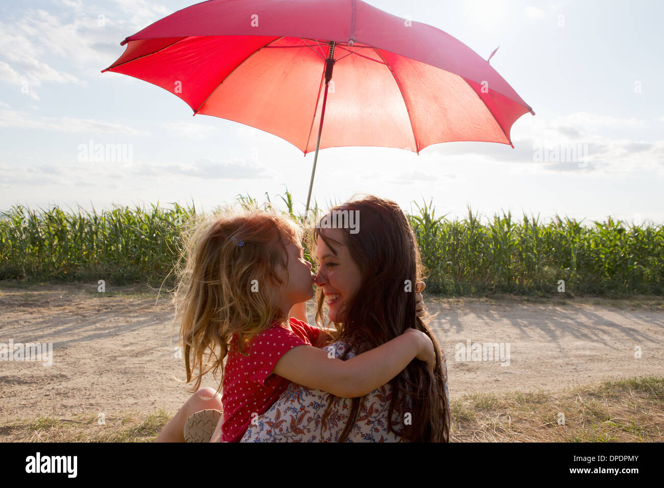 Madre e figlia abbracciando sotto ombrellone rosso Foto Stock