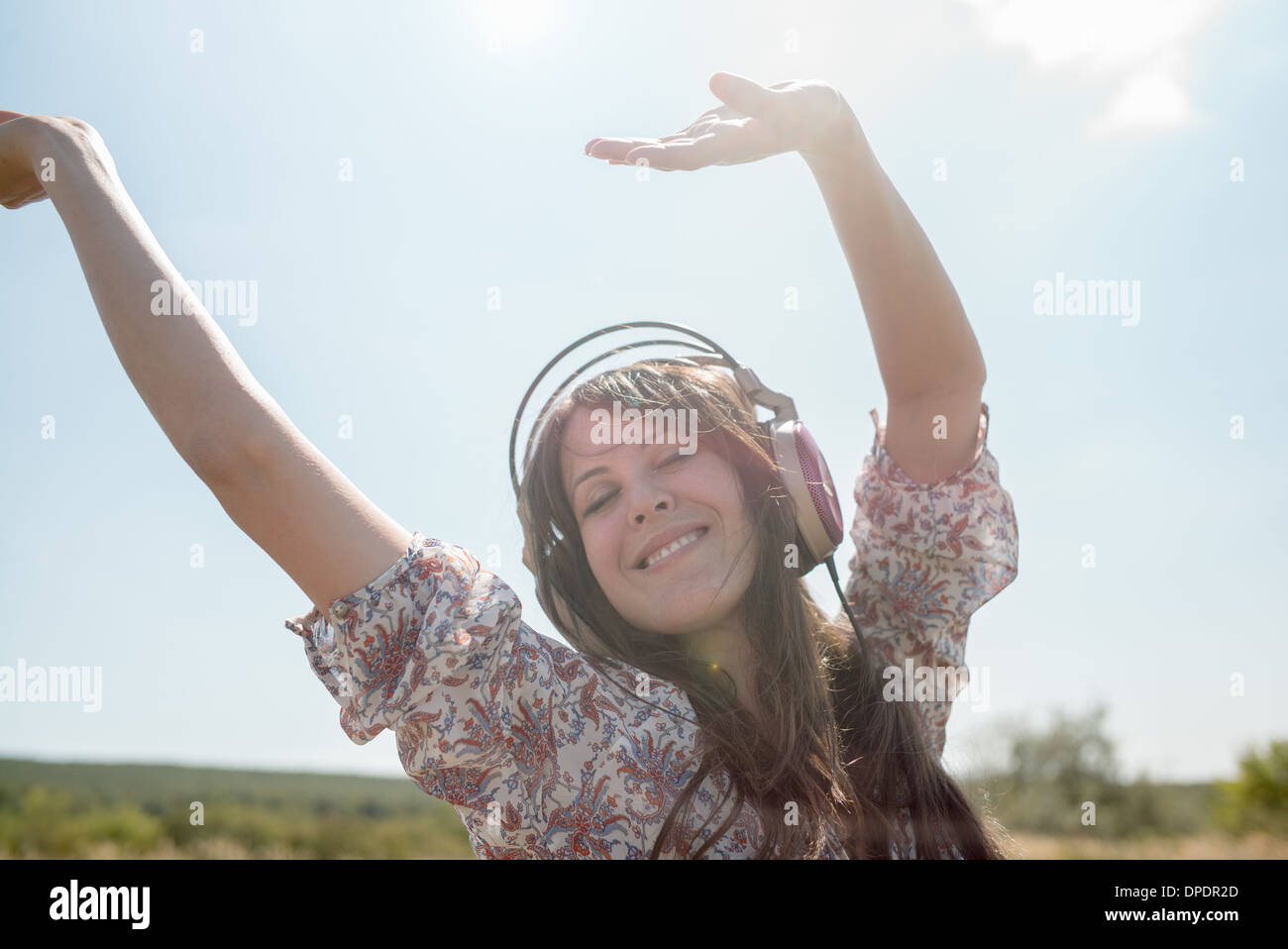 Ritratto di metà donna adulta dancing in campo indossando le cuffie con le braccia sollevate Foto Stock