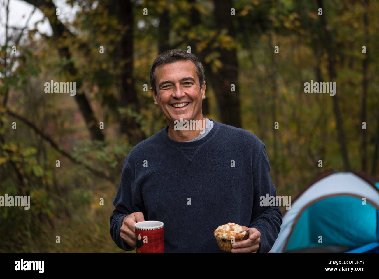 Uomo maturo nella foresta azienda cupcake e bevanda calda Foto Stock