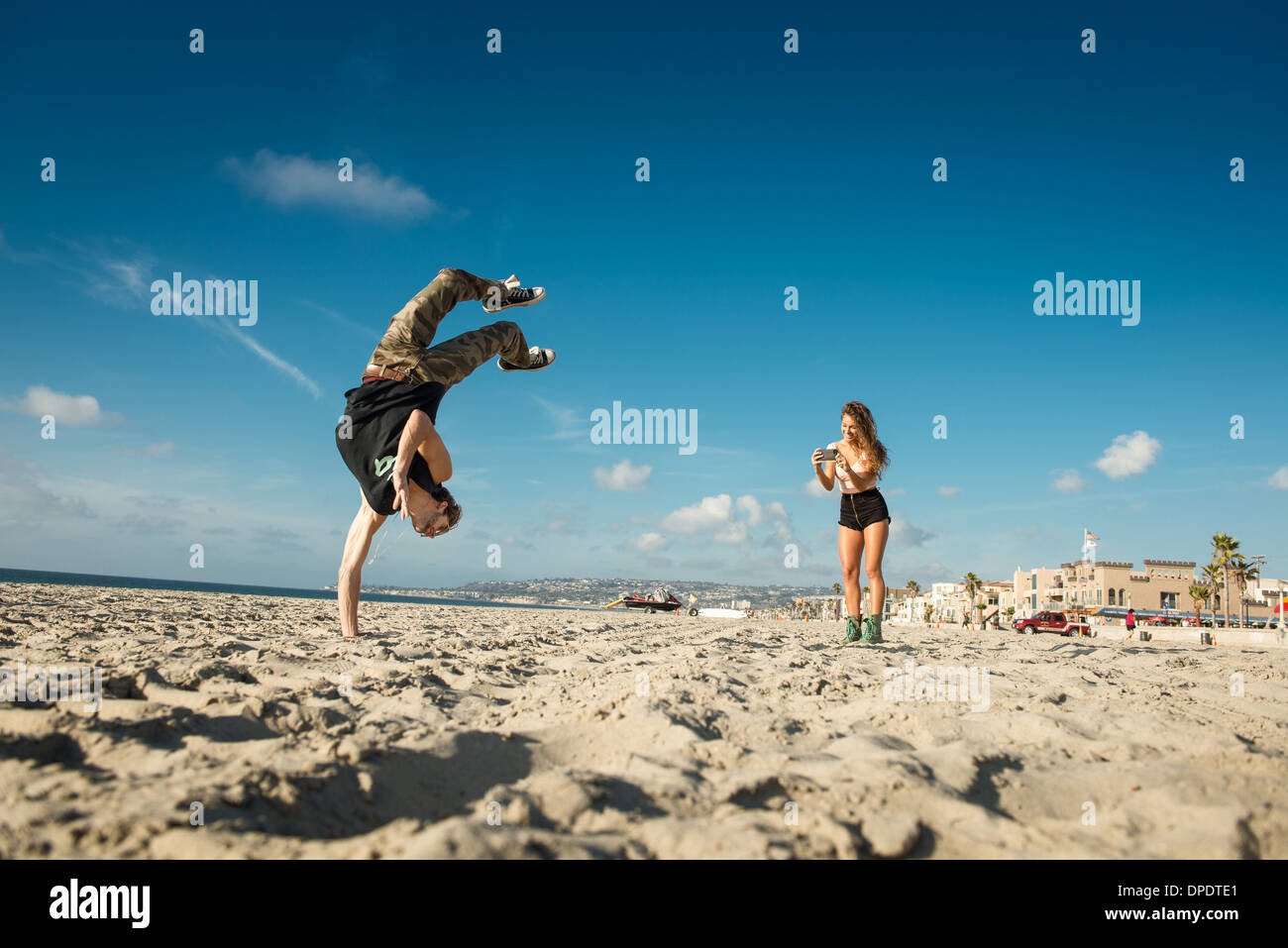 Giovane donna di fotografare il mio ragazzo facendo backflip su San Diego beach Foto Stock