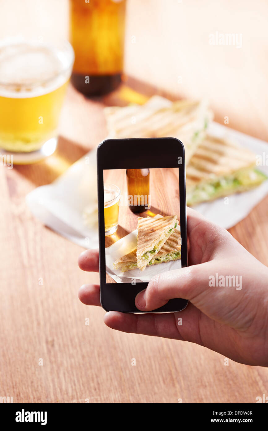 Tenendo lo smartphone foto di formaggio feta panino su un ristorante Foto Stock