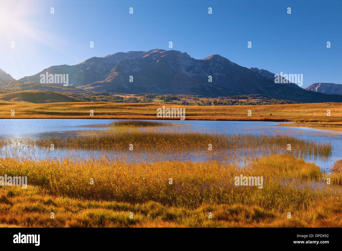 Il lago verso il sole con le montagne sullo sfondo Foto Stock