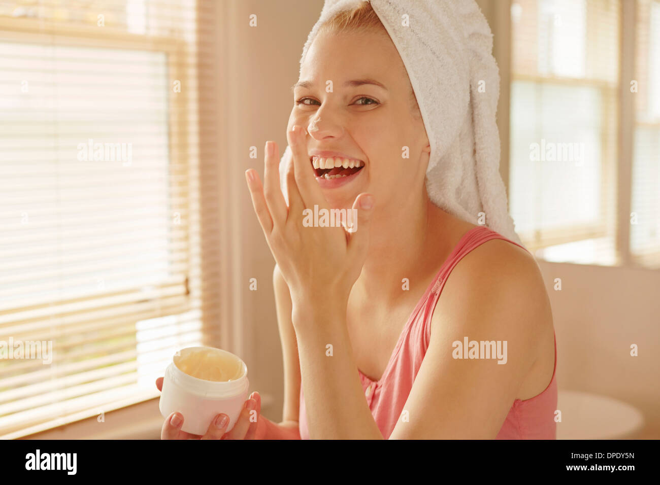 Giovane donna in bagno mettendo in crema per il viso Foto Stock