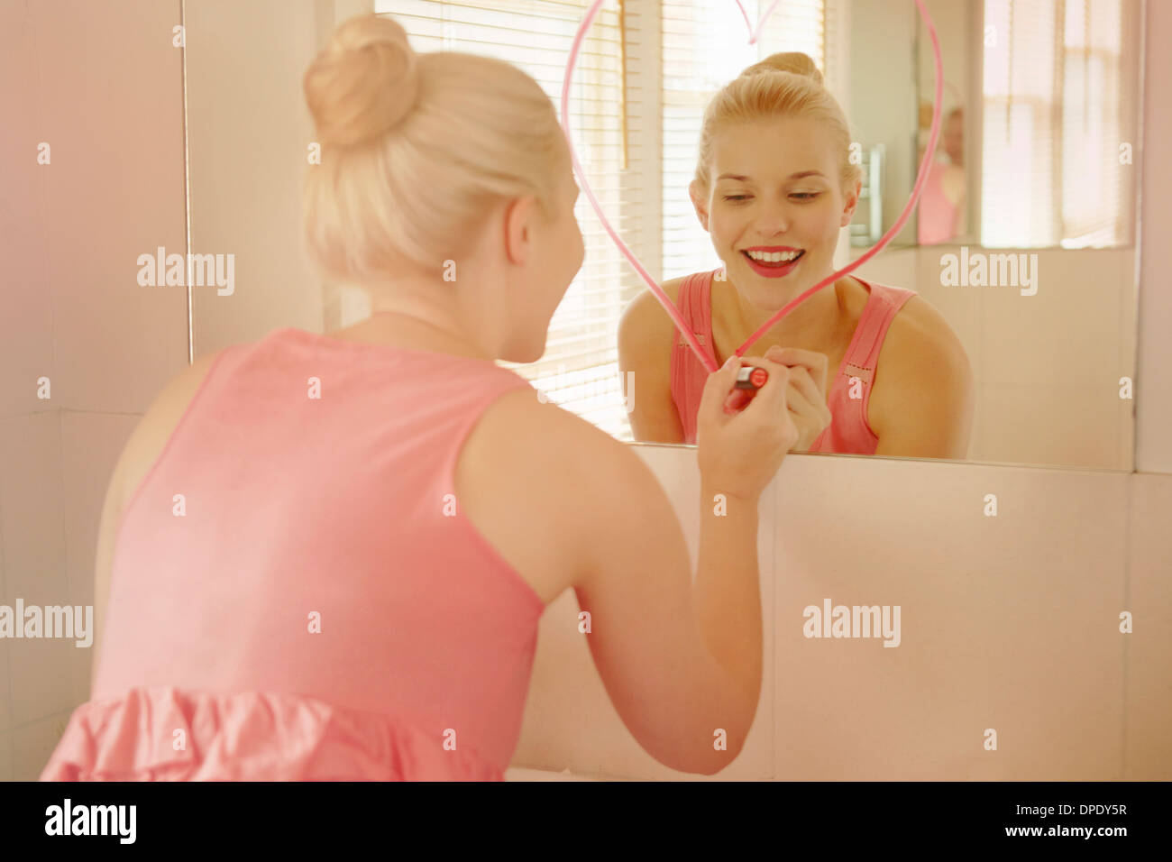 Giovane donna in bagno disegno forma di cuore sullo specchio con il rossetto Foto Stock