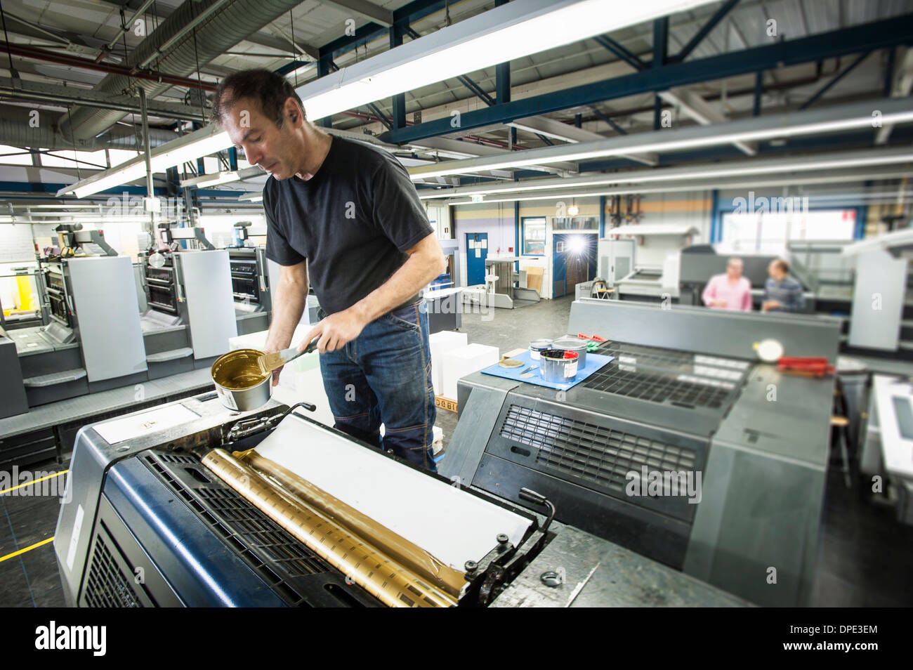 Lavoratore applicando inchiostro oro per macchina da stampa in laboratorio di stampa Foto Stock