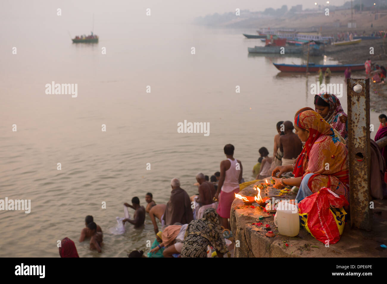 Donna offerte di illuminazione nella parte anteriore dei pellegrini di balneazione all alba del ghats di Varanasi, Uttar Pradesh, India Foto Stock