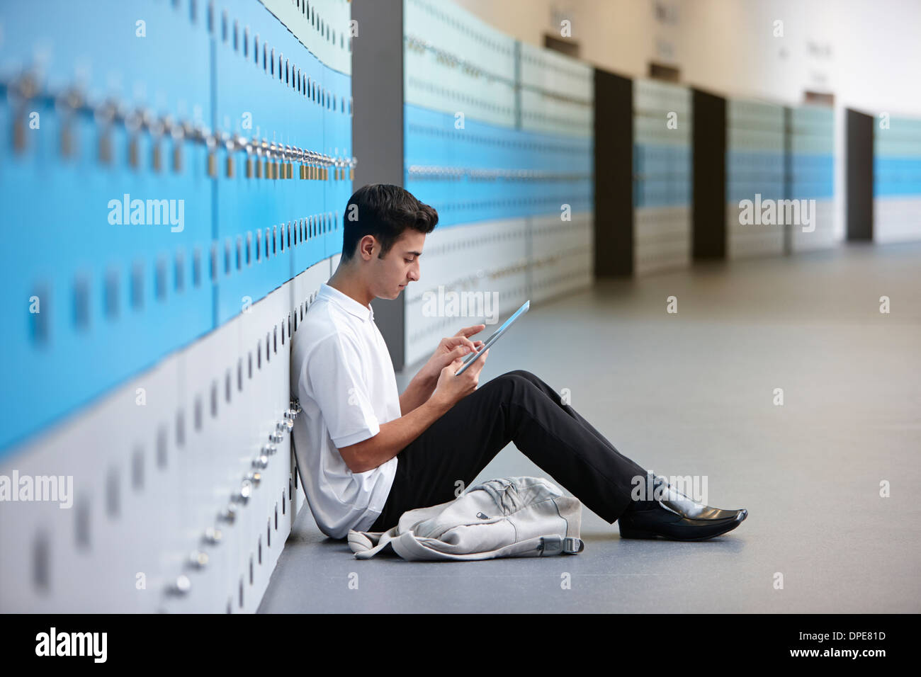 Ritratto di adolescenti schoolboy seduto sul pavimento accanto al di armadietti Foto Stock