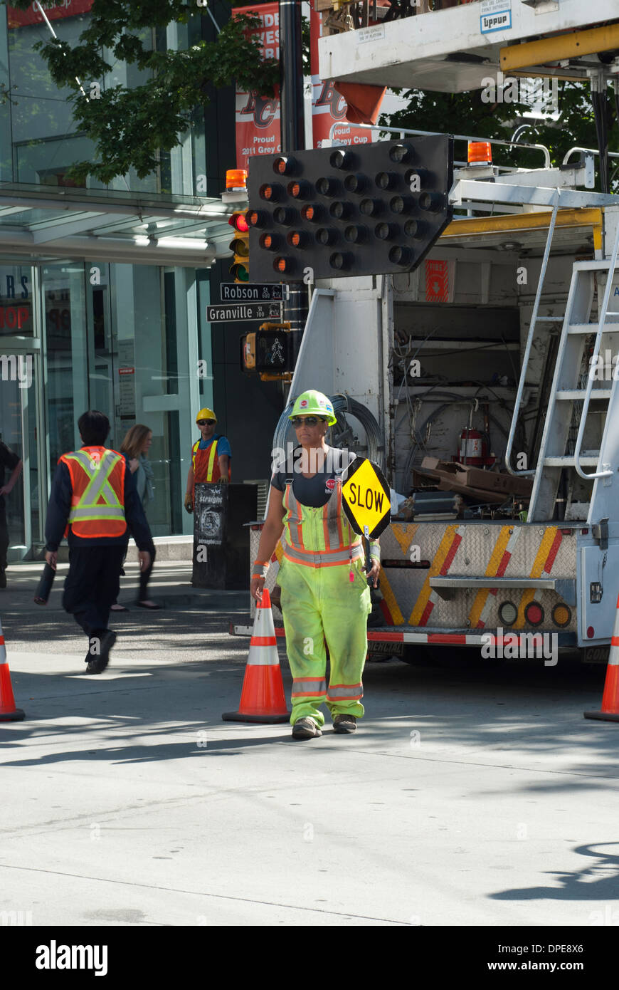 Persona di bandiera tenendo premuto segno lento dirigere il traffico di una città di Vancouver Downtown street. Foto Stock