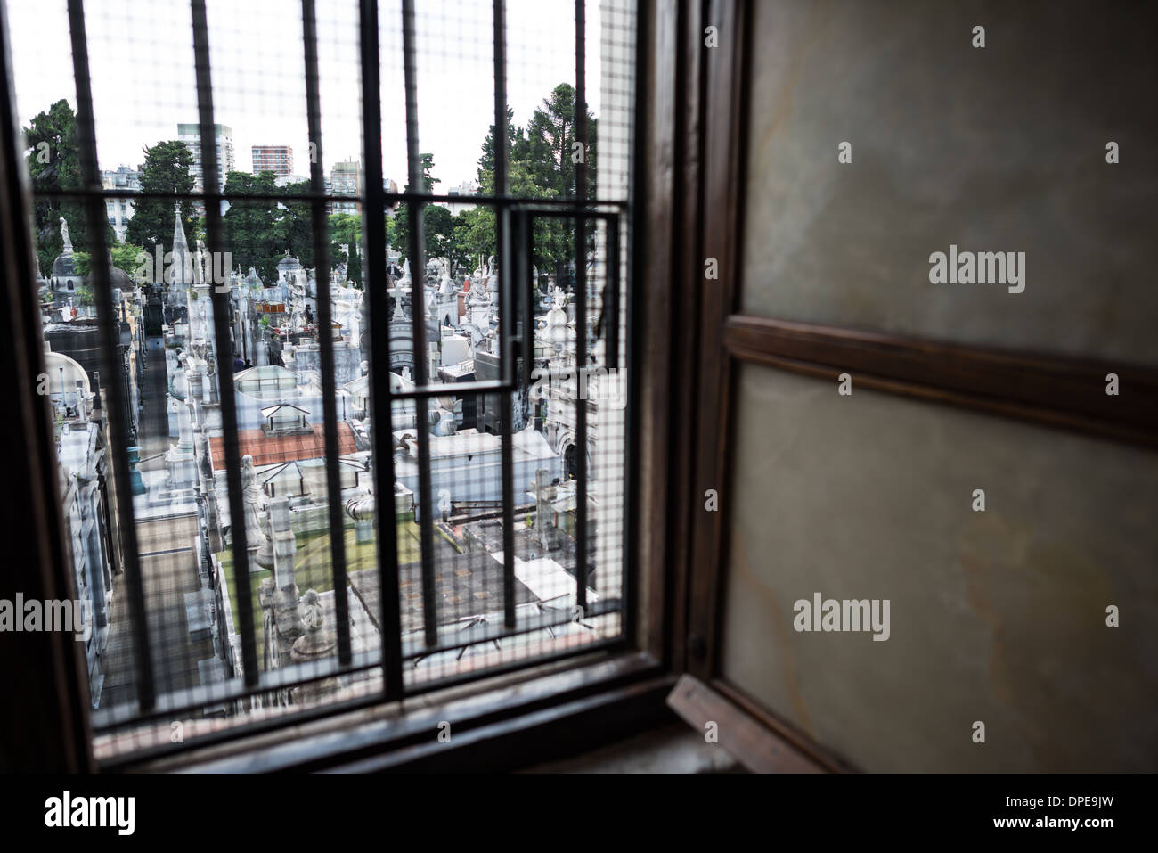 BUENOS AIRES, Argentina: Una vista attraverso una delle finestre originali dell'epoca coloniale della Basílica de Nuestra Señora del Pilar rivela lo storico cimitero di Recoleta oltre. Il cimitero, istituito nel 1822, si trova adiacente alla chiesa del 1732 e si colloca tra i siti storici più significativi di Buenos Aires. Il rapporto architettonico tra questi due monumenti storici esemplifica l'importanza storica del quartiere di Recoleta. Foto Stock