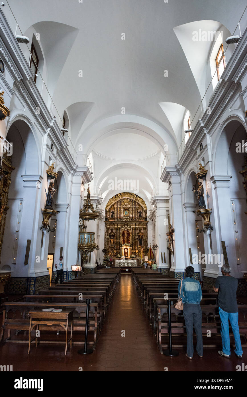 BUENOS AIRES, Argentina - la navata centrale della Basílica de Nuestra Señora del Pilar si estende verso il suo altare barocco decorato, che mostra l'architettura coloniale della chiesa del 1732. Il design a navata singola presenta un transetto sviluppato coperto da volte a vela, dimostrando la classica architettura religiosa coloniale spagnola. Le pareti sono fiancheggiate da pale d'altare e ornamenti barocchi originali, preservando il carattere storico della chiesa. Foto Stock