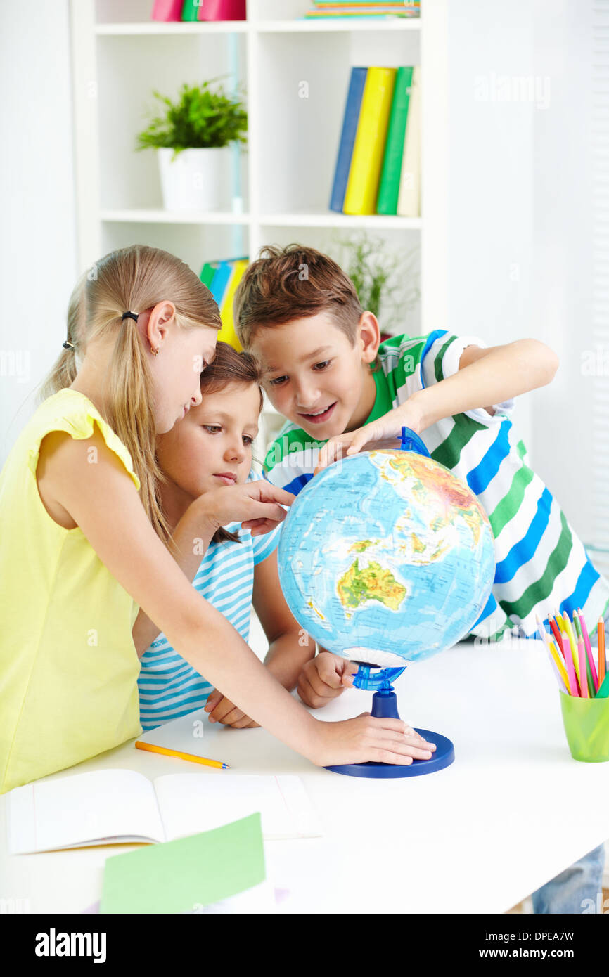 Ritratto di curiosi i compagni di scuola al lavoro studiando globe in aula Foto Stock