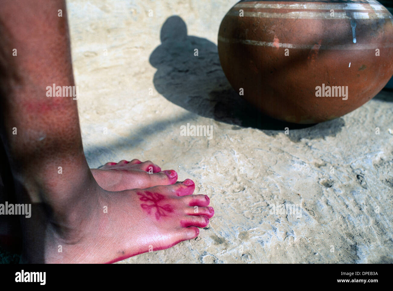 Giovane ragazza si appoggia contro una parete di un edificio sito a Delhi. I suoi piedi sono in modo decorativo dipinto con rosa rosso henné. Foto Stock