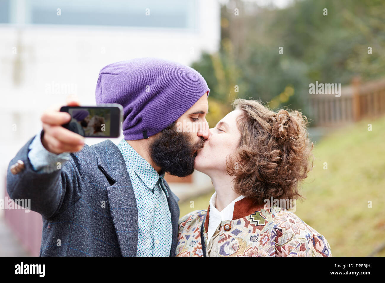 Paio di prendere una fotografia di se stessi baciando con uno smartphone all'aperto Foto Stock