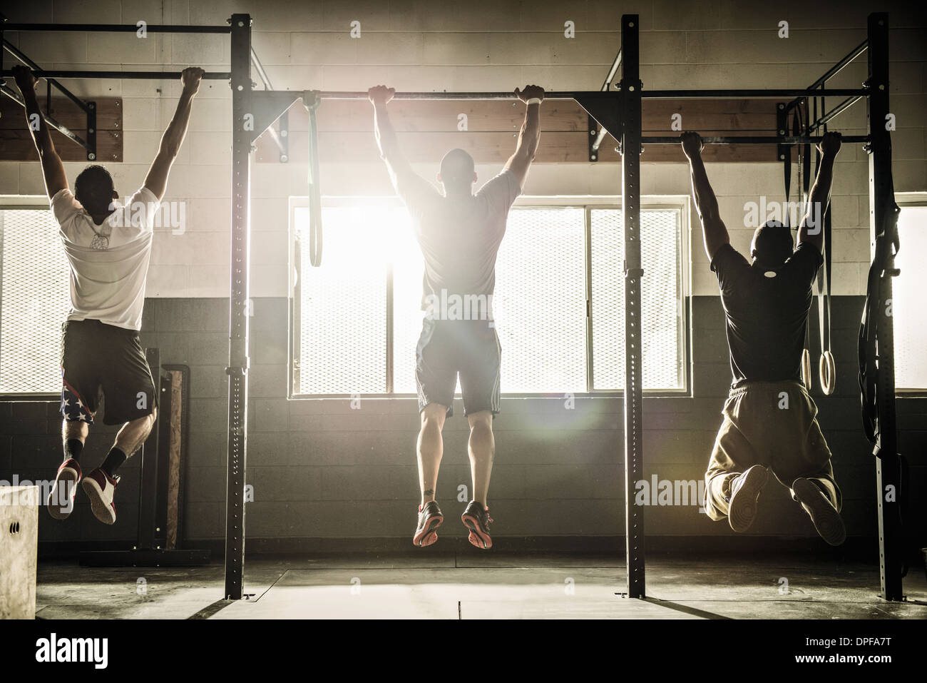 Tre uomini facendo tirare ups sulla barra di esercizio in palestra Foto Stock
