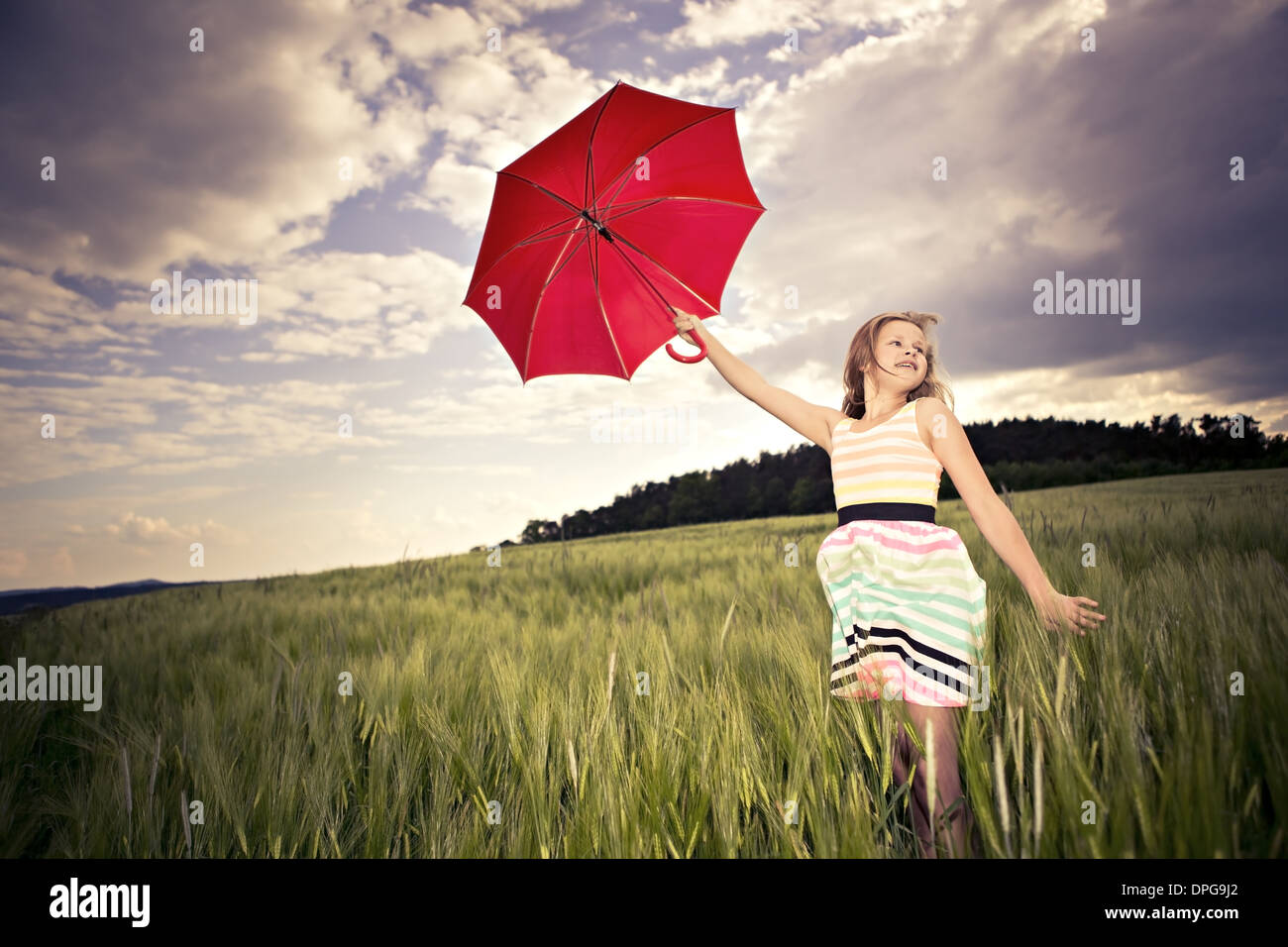 Ragazza adolescente jumping con un ombrello nella parte anteriore del paesaggio rurale Foto Stock