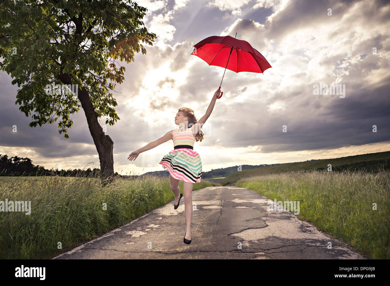 Ragazza adolescente jumping con un ombrello nella parte anteriore del paesaggio rurale Foto Stock