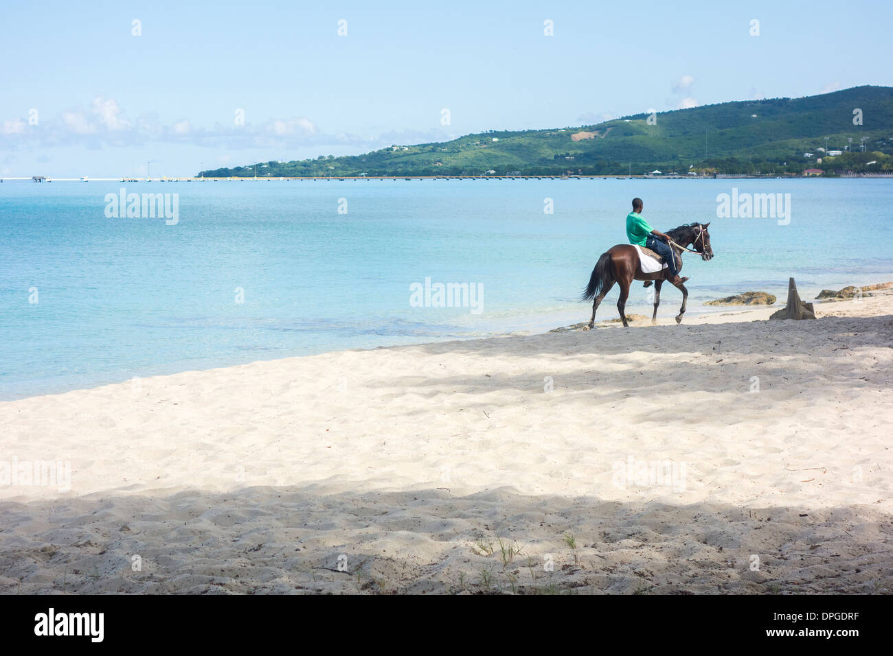 Un nativo di St. Croix, U.S. Isole Vergini cavalca il suo cavallo che è sospettoso occhiatura un castello di sabbia sulla spiaggia di castelli di sabbia. Foto Stock
