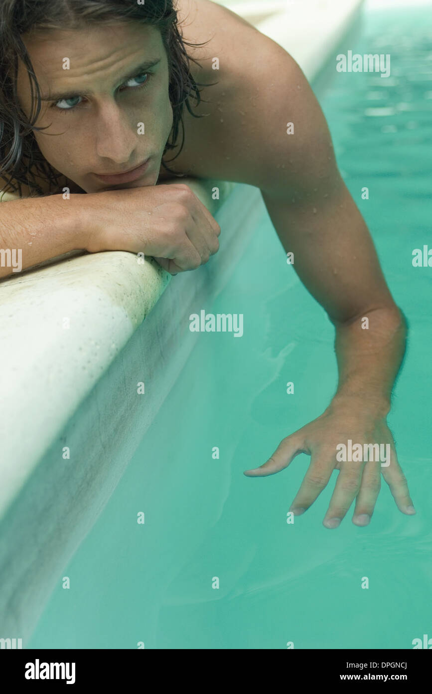 Giovane uomo disteso accanto alla piscina, dondolare il braccio in acqua Foto Stock