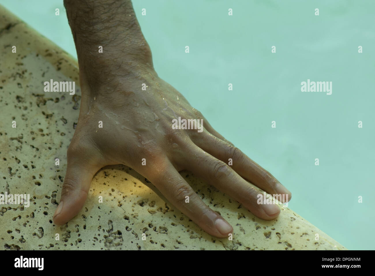 Uomo di mano bagnato sul lato della piscina Foto Stock