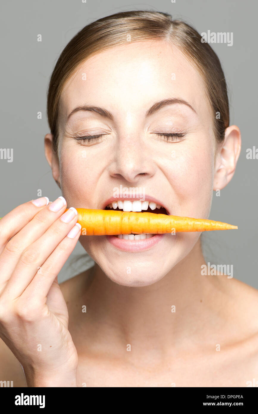Giovane donna di mordere in carota a occhi chiusi Foto Stock