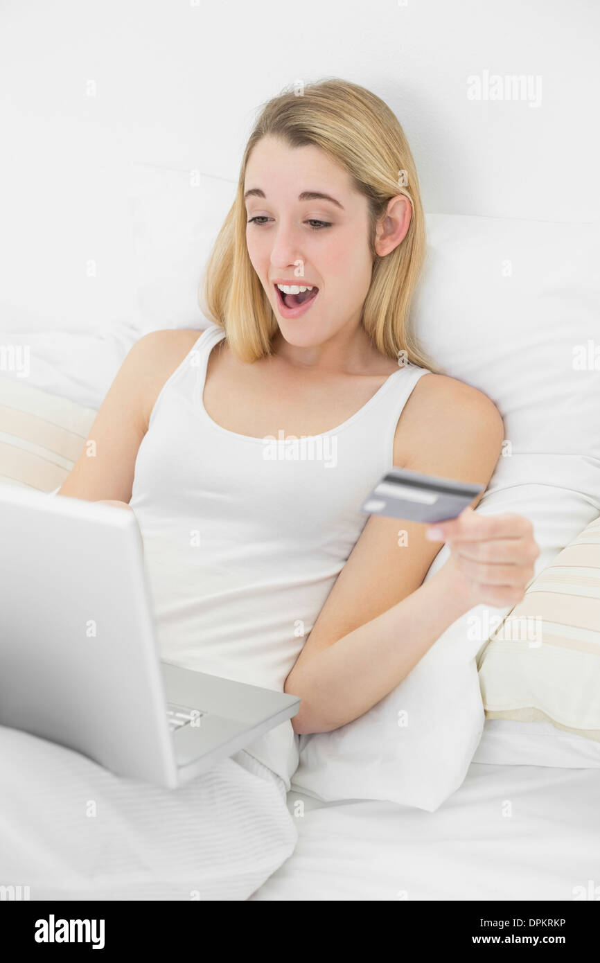 Felice sorpresa donna home shopping con il suo computer portatile sdraiato sul suo letto Foto Stock