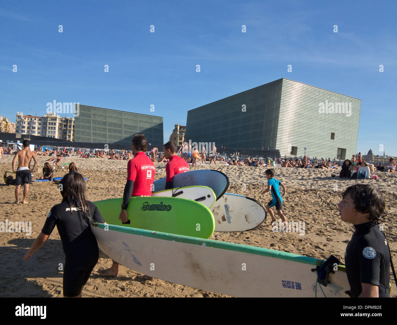 Surfers e lucertole da mare sulla spiaggia Zurriola con centro congressi Kursaal e auditorium in background, San Sebastian, Spagna Foto Stock
