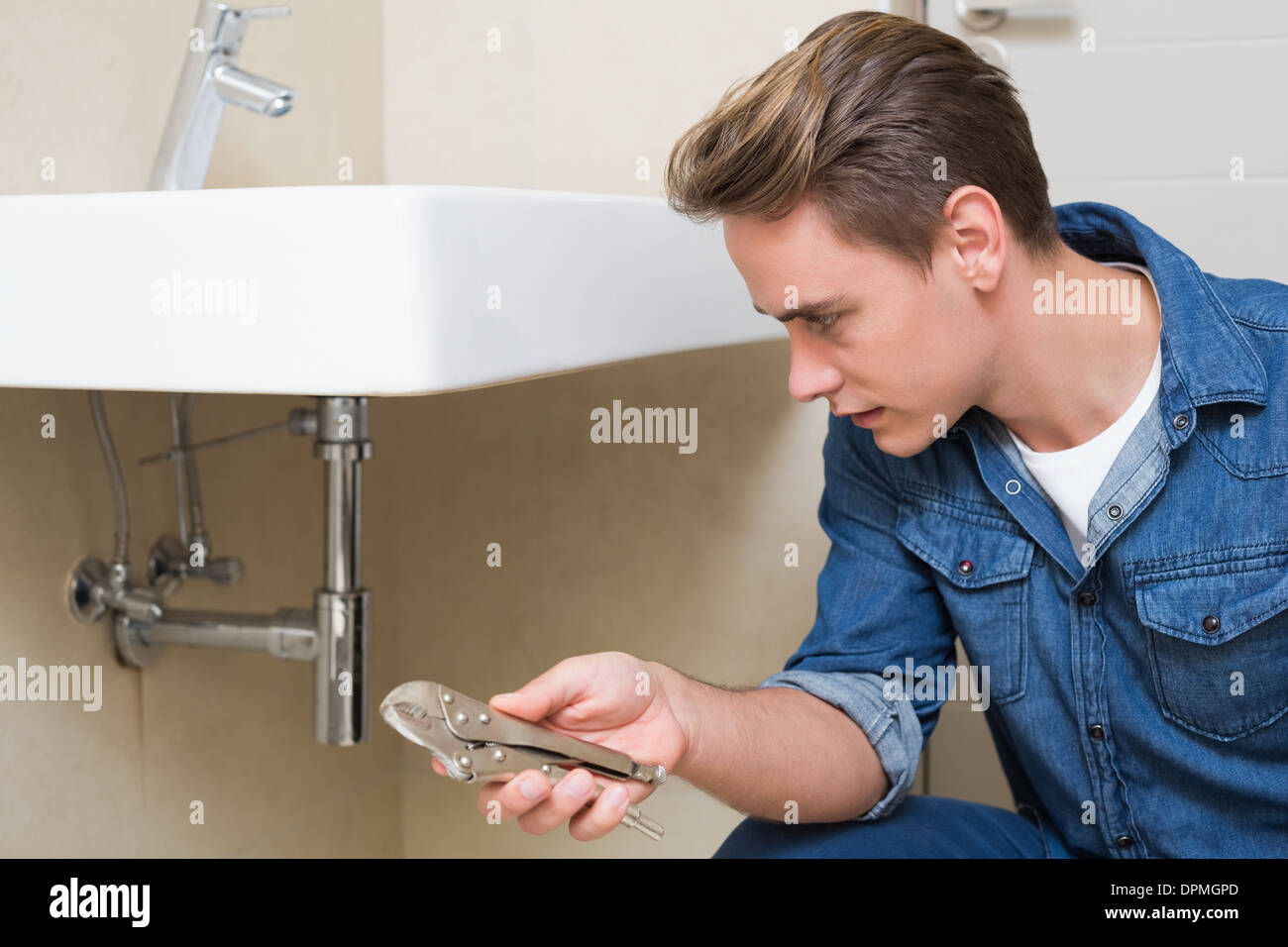 Giovani idraulico con chiave applicando il lavandino in bagno Foto Stock