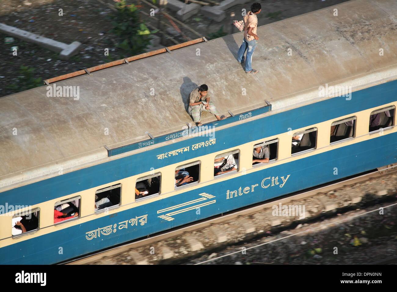 Un uomo in piedi e un'altra seduta sul tetto di una velocità elevata il pendolarismo treno attraverso la città di Dacca in Bangladesh Foto Stock