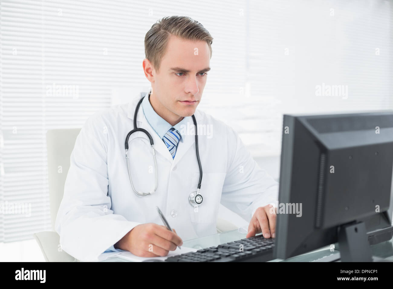Medico a scrivere una nota mentre si utilizza il computer in ufficio medico Foto Stock