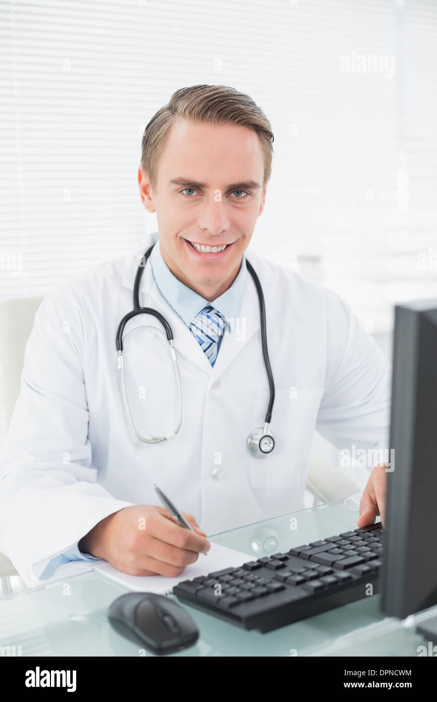 Medico a scrivere una nota mentre si utilizza il computer in ufficio medico Foto Stock