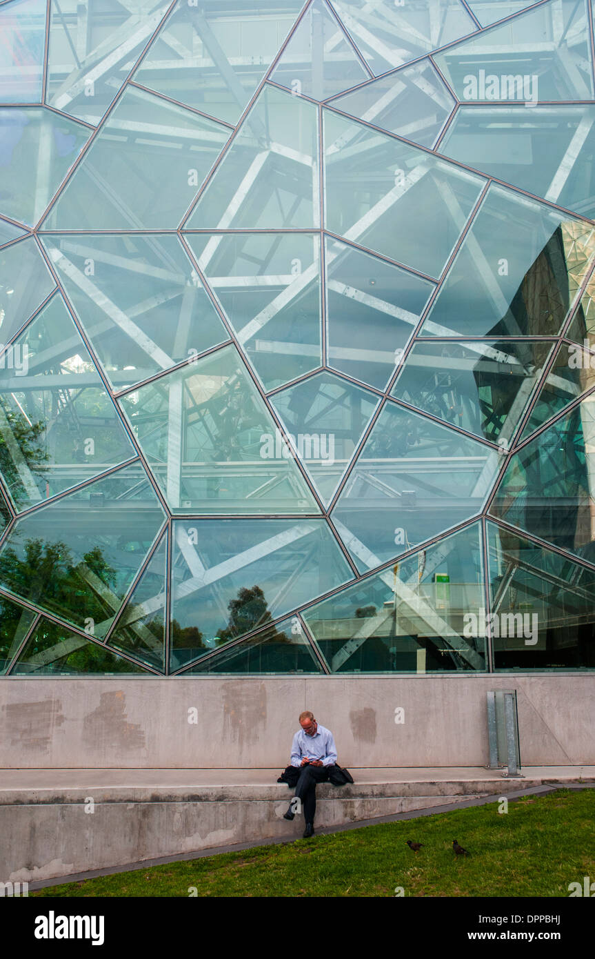 Lettura di uomo al di fuori del bordo Deakin teatro a Federation Square, Melbourne, in una serata estiva Foto Stock
