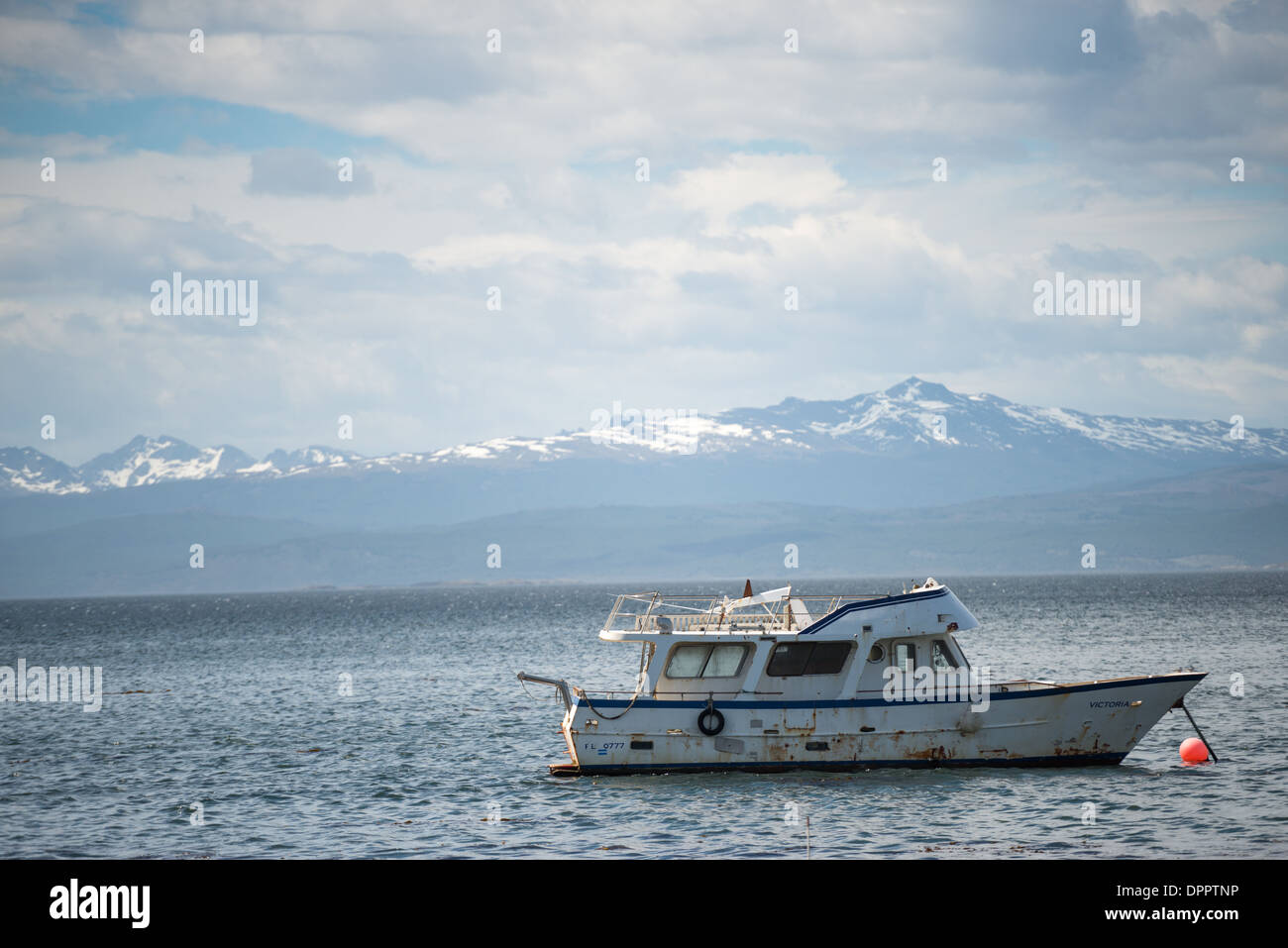 Un ben indossati barca privata è ancorato nel porto di Ushuaia nella parte anteriore del Canale di Beagle. Le montagne innevate in lontananza sono attraverso il Canale di Beagle in Cile. Foto Stock