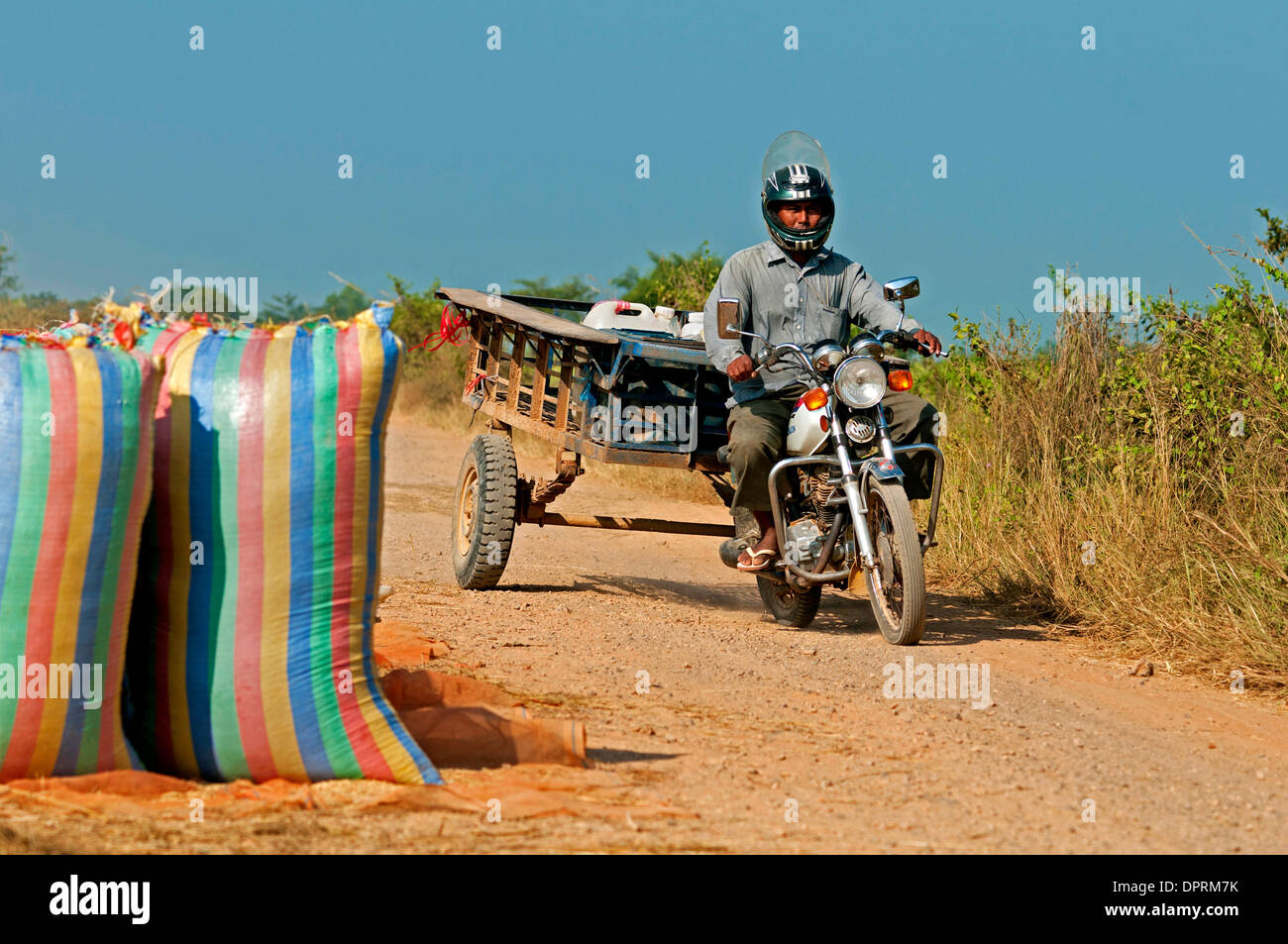 Uomo in moto sulla strada di un paese vicino a Battambang il passaggio di sacchi di riso, Battambang, Cambogia Foto Stock