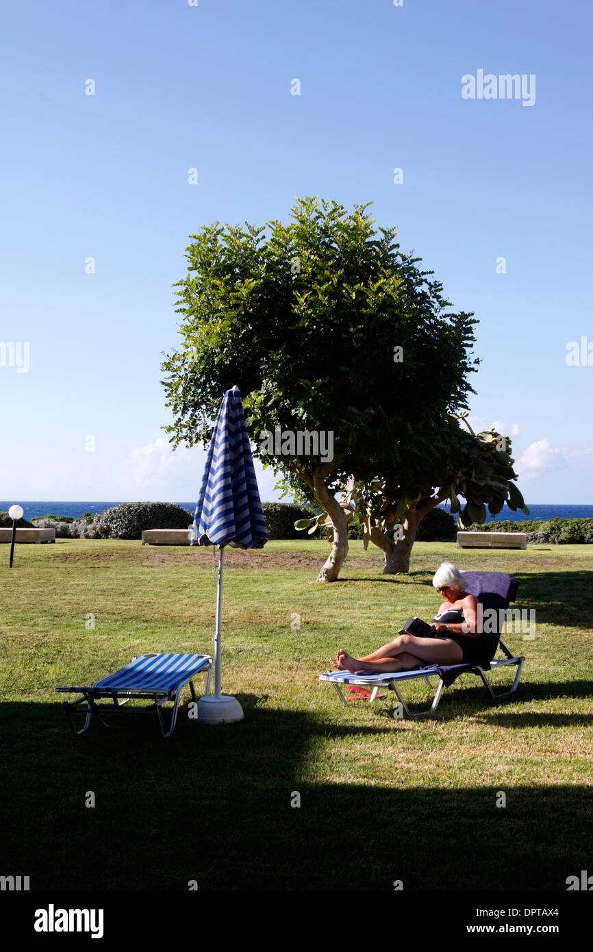 Una donna di lettura su un lettino in un giardino dell'hotel. Creta. Foto Stock