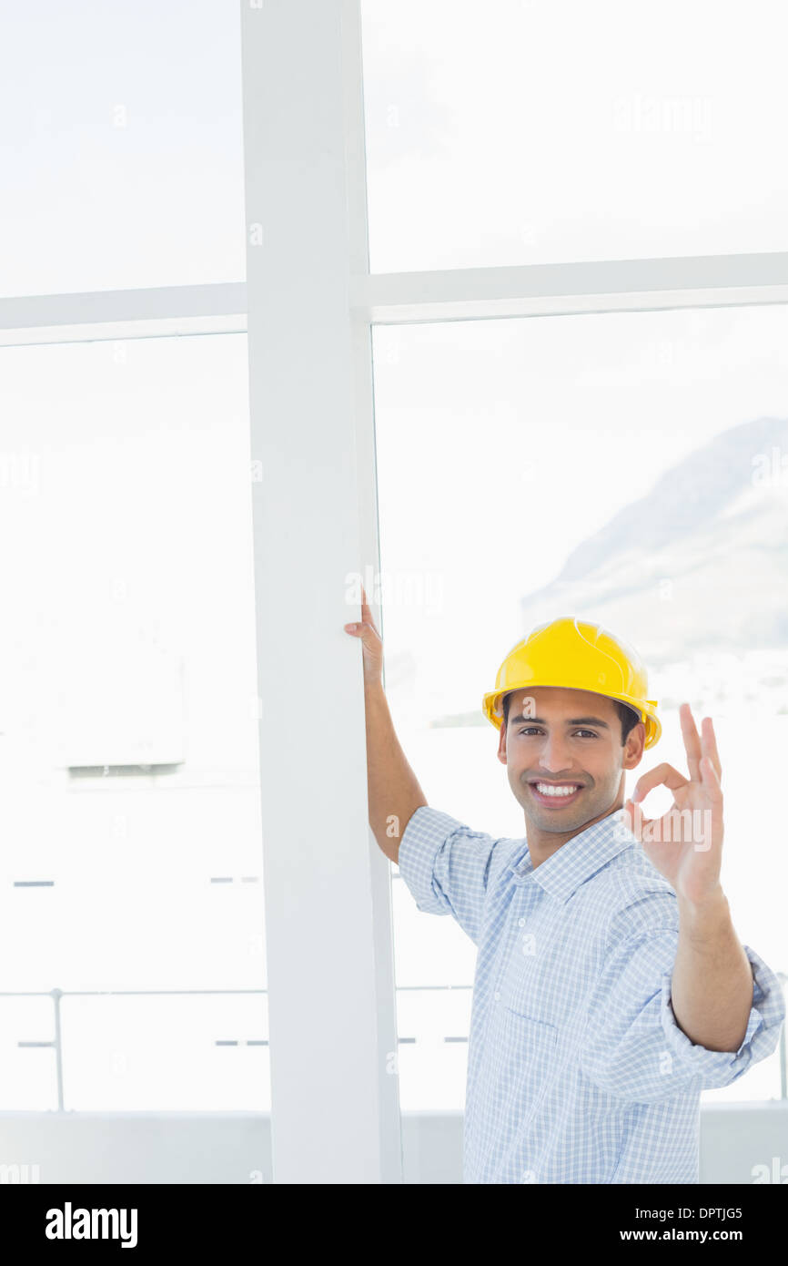 Tuttofare in giallo elmetto gesticolando okay sign in office Foto Stock