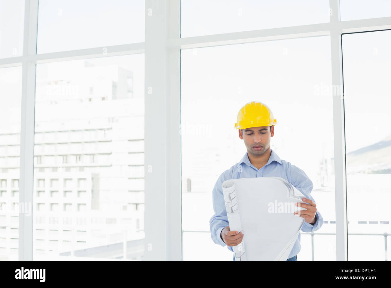 Architetto nel casco giallo guardando blueprint in office Foto Stock