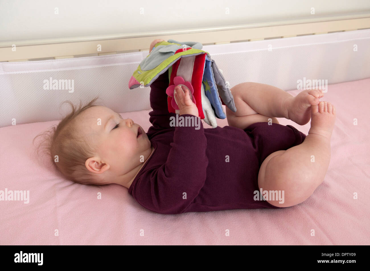 Bambina che giace nella sua culla e giocando con un panno morbido prenota Foto Stock