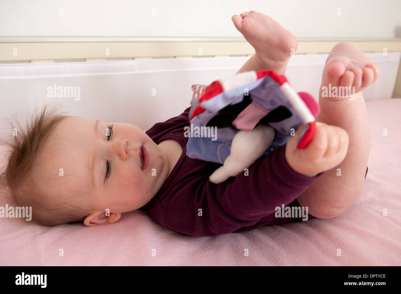 Bambina che giace nella sua culla e giocando con un panno morbido prenota Foto Stock