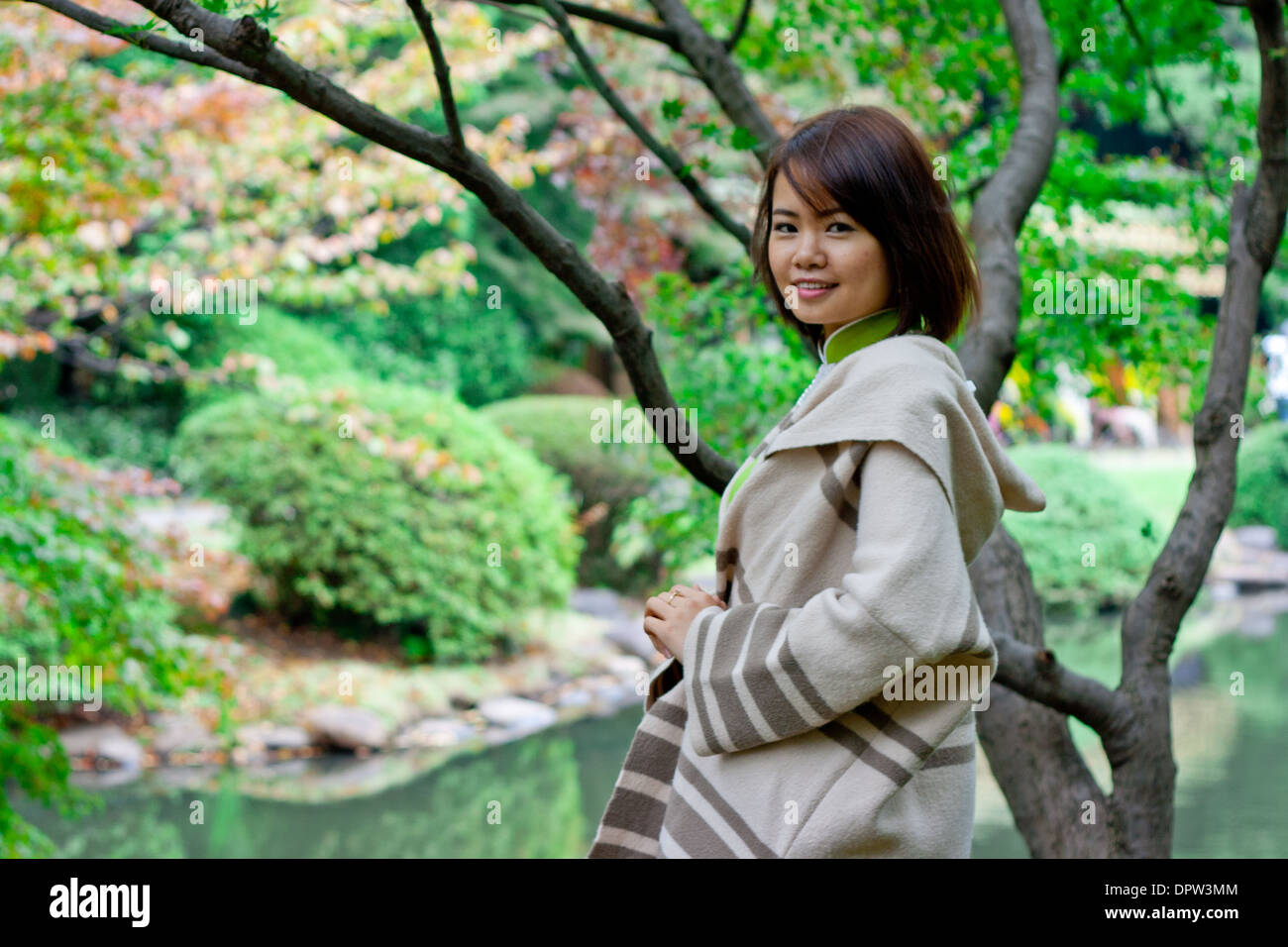 Ritratto di giovane donna sorridente in telecamera in un parco di fronte a un lago Foto Stock