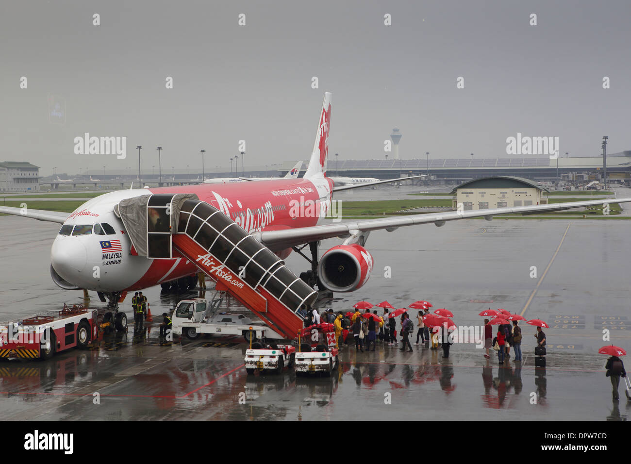 Imbarco passeggeri Air Asia airlines volo utilizzando la scala nella pioggia, con ombrelloni rosso fornito dalla compagnia aerea Foto Stock