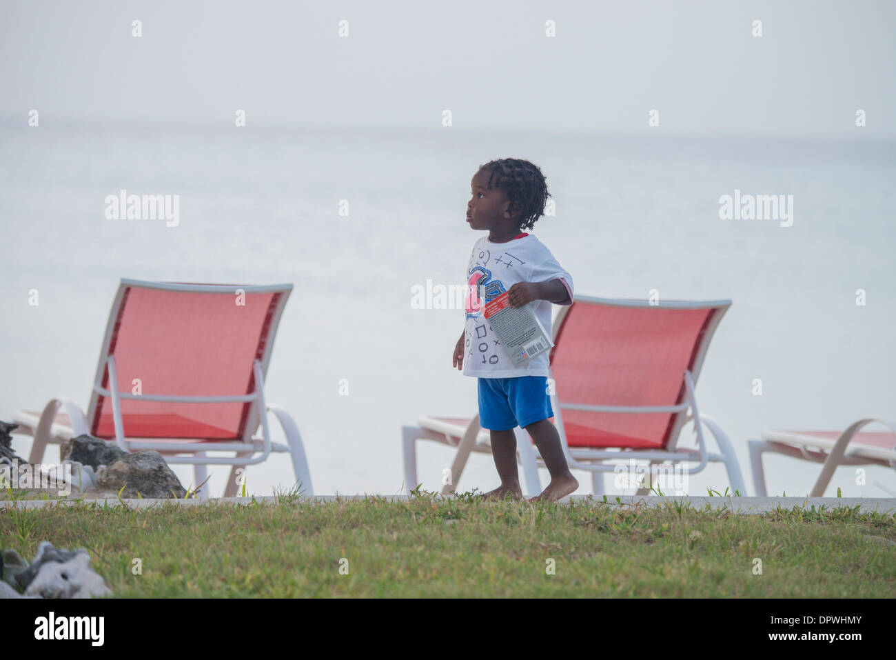 Un bimbo African American boy porta un libro sulla riva di St. Croix, U.S. Isole Vergini. Foto Stock